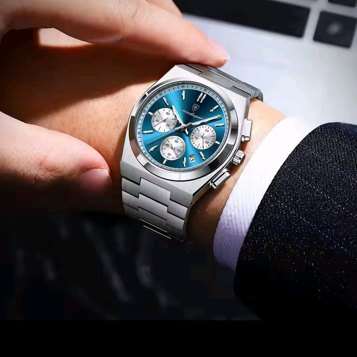 Hand wearing a silver watch with a blue face on a dark background